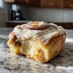 Close-up of an irresistible gingerbread spice cinnamon roll with creamy maple frosting and a bite taken out.