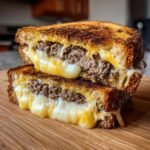 A close-up of an Irresistible Patty Melt Recipe, showing perfectly grilled bread with melted cheese oozing out and a juicy beef patty inside.