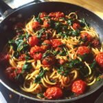 A close-up of Irresistible Tomato Spinach One Pot Pasta in a pan, with whole cherry tomatoes and wilted spinach.