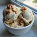 Close-up of three scoops of Maple Brown Butter Walnut Ice Cream topped with whole and crushed walnuts in a white bowl.