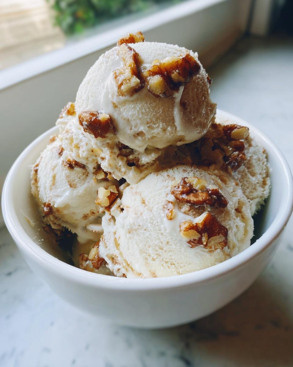 Three scoops of creamy Maple Brown Butter Walnut Ice Cream topped with candied walnuts in a white bowl.