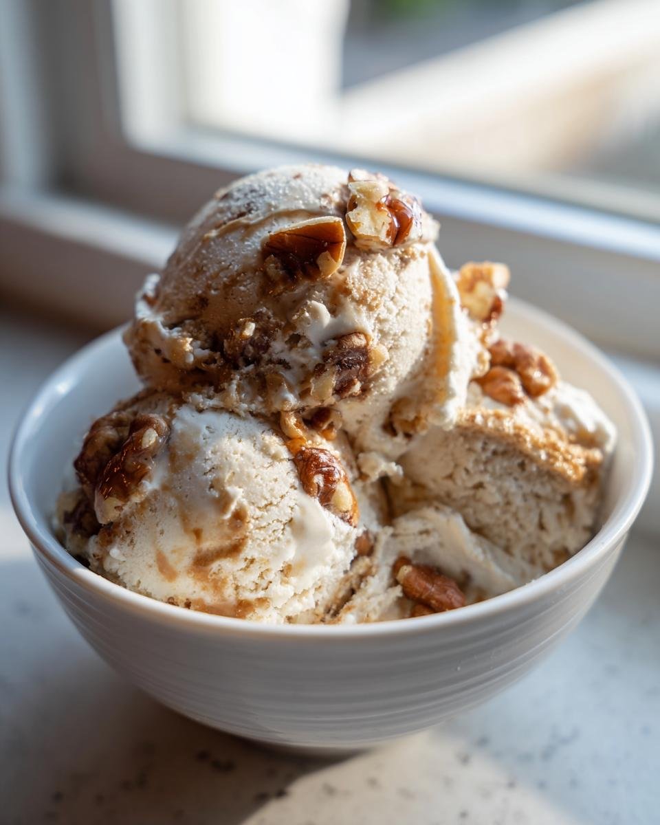 Three scoops of Maple Brown Butter Walnut Ice Cream topped with candied walnuts in a white bowl.