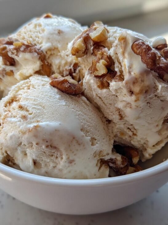 Three scoops of Maple Brown Butter Walnut Ice Cream topped with toasted walnuts in a white bowl.