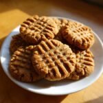 A stack of freshly baked Melt In Your Mouth Peanut Butter Cookies with classic crisscross fork marks on a white plate.