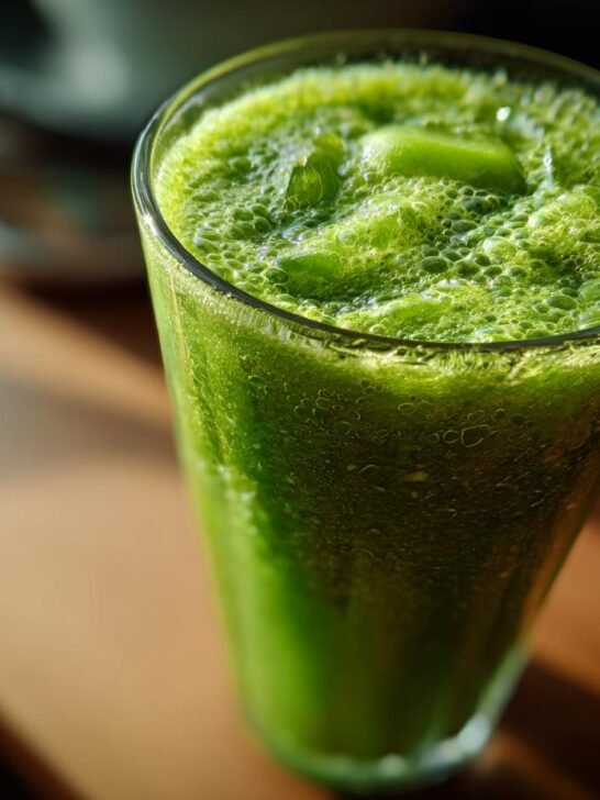 A tall glass filled with vibrant green Morning Glory Detox Juice, topped with foam and ice.