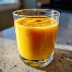 A refreshing Morning Mango Tropical Smoothie in a clear glass, with visible chia seeds and a bright orange hue.