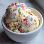 Two scoops of My Favorite Funfetti Cake Ice Cream in a white bowl, topped with colorful sprinkles.