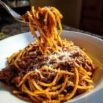 A fork lifting a generous portion of My Grandma's Weeknight Spaghetti, topped with rich meat sauce and grated Parmesan cheese.