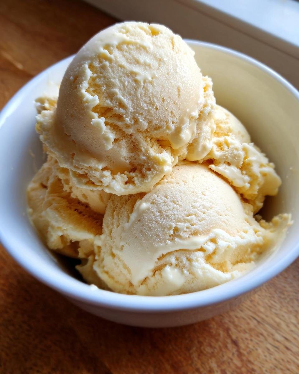 A white bowl filled with scoops of creamy, pale yellow no churn banana ice cream.