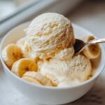 A bowl of creamy, no-churn banana ice cream with fresh banana slices and a spoon.