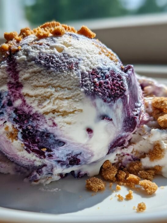 Close-up of a scoop of No Churn Blueberry Protein Ice Cream swirled with blueberry puree and topped with gingersnap crumbles.