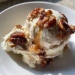 A close-up of a scoop of creamy No Churn Butter Pecan Ice Cream topped with candied pecans and syrup.