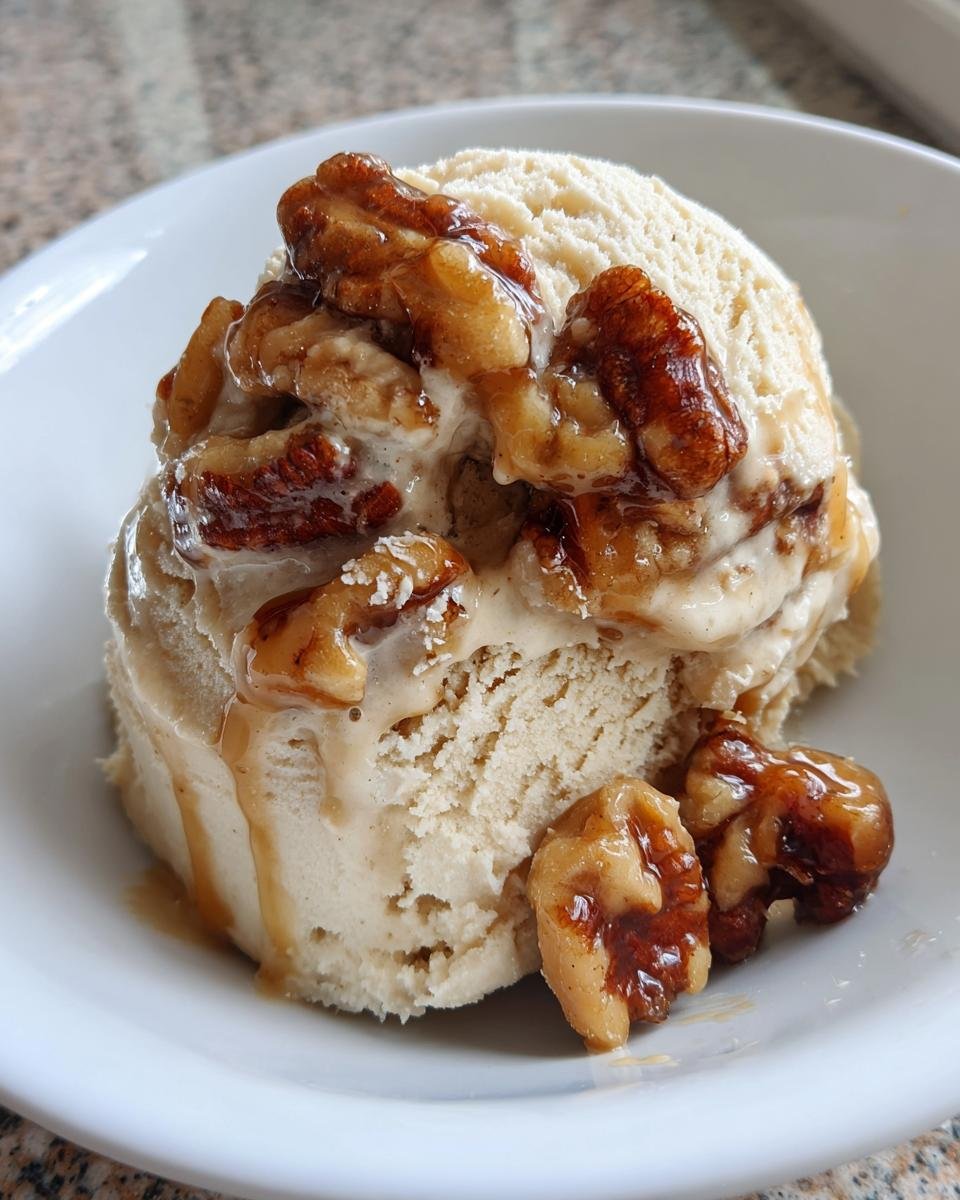 A scoop of creamy No Churn Butter Pecan Ice Cream topped with glazed pecans and caramel drizzle in a white bowl.