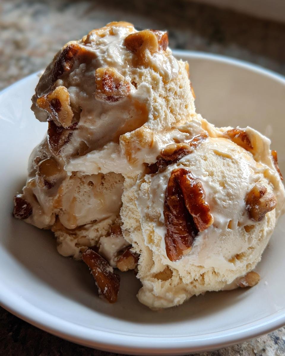 Two scoops of creamy No Churn Butter Pecan Ice Cream topped with candied pecans, served in a white bowl.