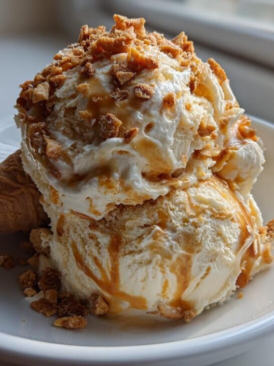 Two scoops of No Churn Caramel Cone Ice Cream drizzled with caramel and topped with crunchy bits, served with a waffle cone piece.