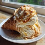 Two scoops of No Churn Caramel Cone Ice Cream drizzled with caramel and topped with crunchy bits in a waffle cone.