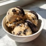 Three scoops of No Churn Peanut Butter Oreo Ice Cream studded with cookie pieces and garnished with whole Oreos in a white bowl.