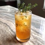 A tall glass filled with a bubbly, amber Pear Ginger Lemon Thyme Drink, garnished with fresh thyme sprigs.
