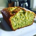 A close-up view of a freshly baked Pesto Zucchini Bread loaf, showing the moist, green interior flecked with zucchini.