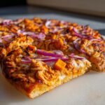 A slice of Pumpkin BBQ Chicken Pizza With Butternut Squash topped with red onions and melted cheese.