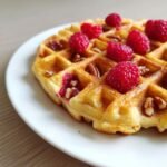Close-up of a golden Raspberry Pecan Vegan Waffles topped with fresh raspberries and pecans.