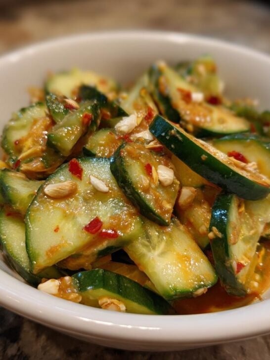 Close-up of sliced cucumbers coated in a spicy peanut sauce with chili flakes and peanuts.