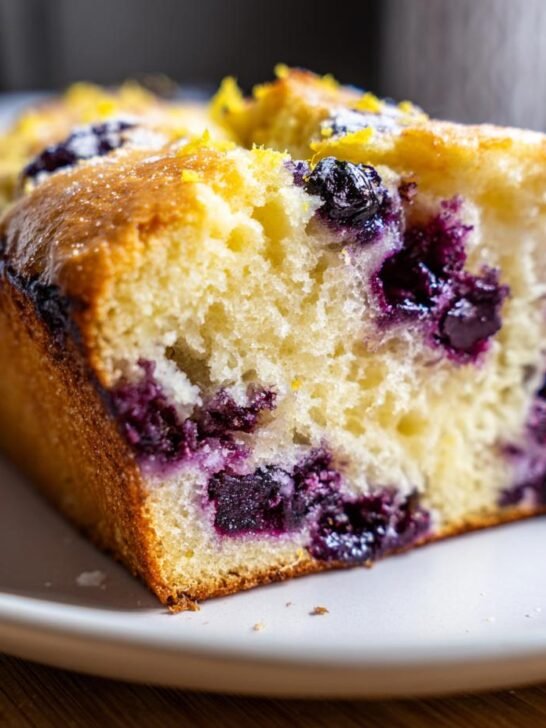 Close-up of a moist slice of Roasted Blueberry Lemon Olive Oil Bread showing plump blueberries and lemon zest topping.