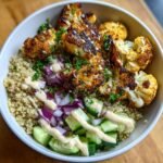 A close-up of Savory Cauliflower Shawarma Bowls with roasted cauliflower, quinoa, cucumber, red onion, and a drizzle of tahini sauce.