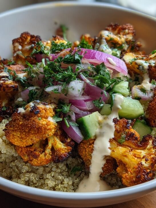 A close-up of Savory Cauliflower Shawarma Bowls, featuring roasted cauliflower florets over quinoa with cucumber, red onion, and a creamy tahini dressing.