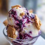 Two scoops of creamy Southern Blackberry Cobbler Ice Cream swirled with blackberry sauce and topped with cookie pieces.