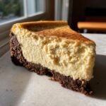 A rich slice of Spiced Chai Cheesecake Gingersnap Crust dusted with cinnamon.