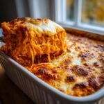 A serving being lifted from a baked dish, showing melted, stringy cheese over the Spicy Pumpkin Pasta Bake.
