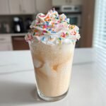 A tall glass of a blended Sugar Cookie Mocktail topped with whipped cream and colorful sprinkles.