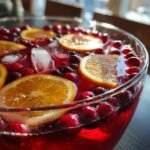 Close-up of a bright red Thanksgiving Punch in a glass bowl, garnished with orange slices, fresh cranberries, and ice cubes.