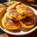 A stack of thick fluffy sweet potato pancakes dusted with cinnamon on a white plate.