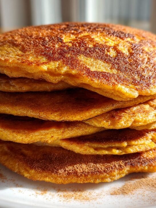 A stack of Thick Fluffy Sweet Potato Pancakes dusted with cinnamon on a white plate.