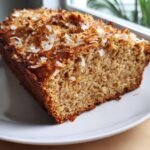 Close-up of a slice of moist Toasted Coconut Bread Gluten Free topped with toasted coconut flakes.