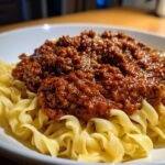 A close-up shot of rich, dark red Vegan Bolognese sauce generously spooned over wavy egg-free pasta noodles.