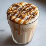 Close-up of a creamy Vegan Caramel Eggnog Mocktail topped with foam, caramel drizzle, and chocolate shavings.