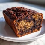 A close-up of a freshly baked Vegan Chocolate Bourbon Banana Bread loaf topped with melted chocolate chips.