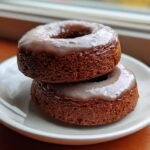 Two stacked Vegan Gingerbread Donuts Chai Glaze on a white plate near a window.