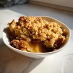 Close-up of a single serving of Vegan Gluten Free Apple Crisp with golden brown topping in a white bowl.