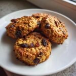 Four golden-brown Vegan Superfood Breakfast Cookies studded with dark raisins, served on a white plate.
