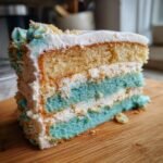 A slice of vegan vanilla dinosaur birthday cake with blue and white frosting and layers.