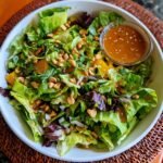 A vibrant Zesty Salad With Asian Dressing, featuring fresh greens, oranges, peanuts, and a side of dressing.