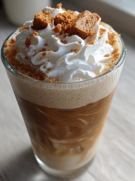 Close-up of a tall glass of Biscoff Cookie Iced Coffee topped with whipped cream and cookie crumbles.