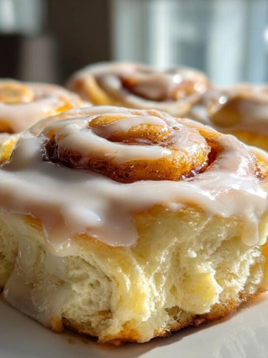 Close-up of fluffy Apple Butter Cinnamon Rolls topped with thick white icing dripping down the sides.