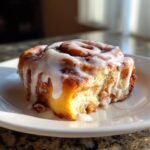 A close-up of a gooey, freshly baked Apple Cider Cinnamon Rolls covered in thick white icing.