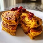 Close-up of a stack of fluffy Apple Cider Pumpkin Pancakes Cranberries, cut open to show texture and dried cranberries.