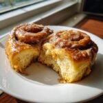 Two soft Apple Pie Cinnamon Rolls, one broken open to show the fluffy interior, covered in sweet glaze.